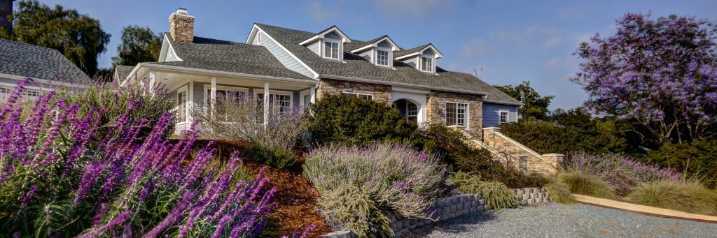 Image of a beautiful Cape Cod style home located in Fallbrook California. The home features a beautiful water-wise landscape in full spring bloom.